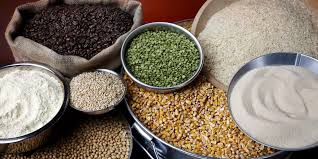 Variedade de grãos e farinhas dispostos em recipientes e sacos, incluindo milho, arroz, feijão, soja, farinha de trigo, grão-de-bico e lentilha.